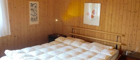 Et værelse med træpaneler, en seng, et natbord og en lampe fastgjort til væggen.