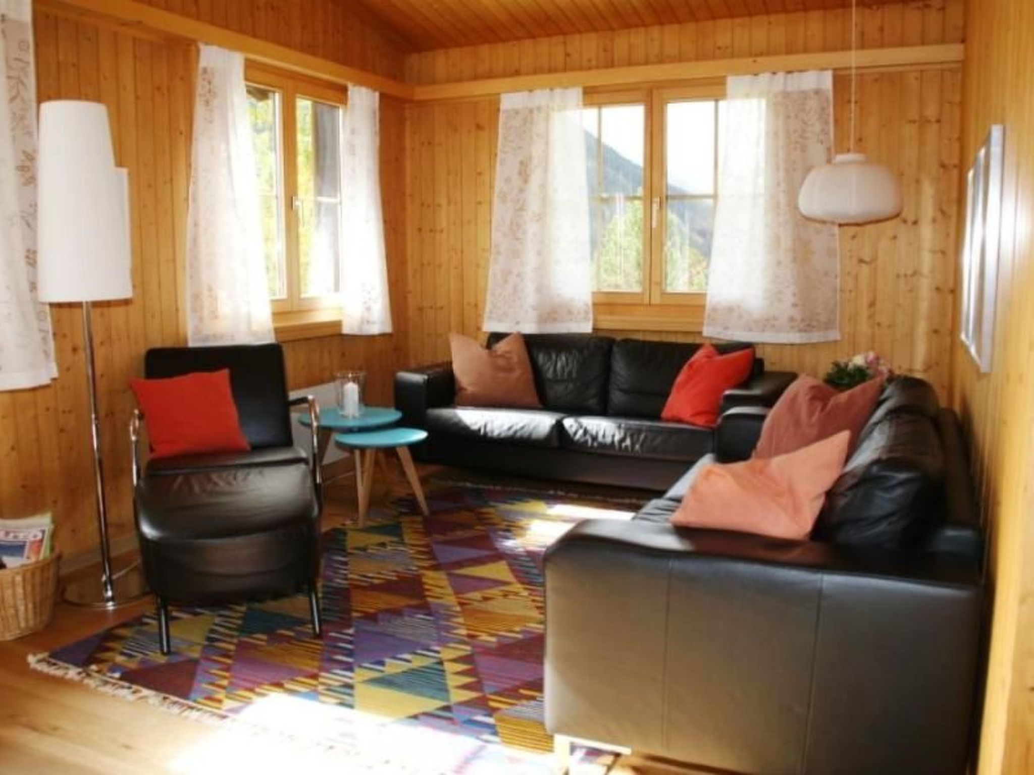 A cozy living room with a black leather sofa, a small round table, and a colorful rug.