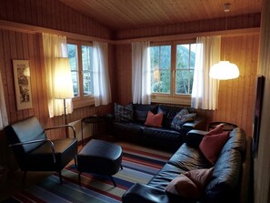A cozy room with a sofa, a chair, and a table. There are windows with curtains, and a lamp hangs from the ceiling. - Ferienhaus Kuster, (Sedrun), 006.01 by Interhome (Sedrun)