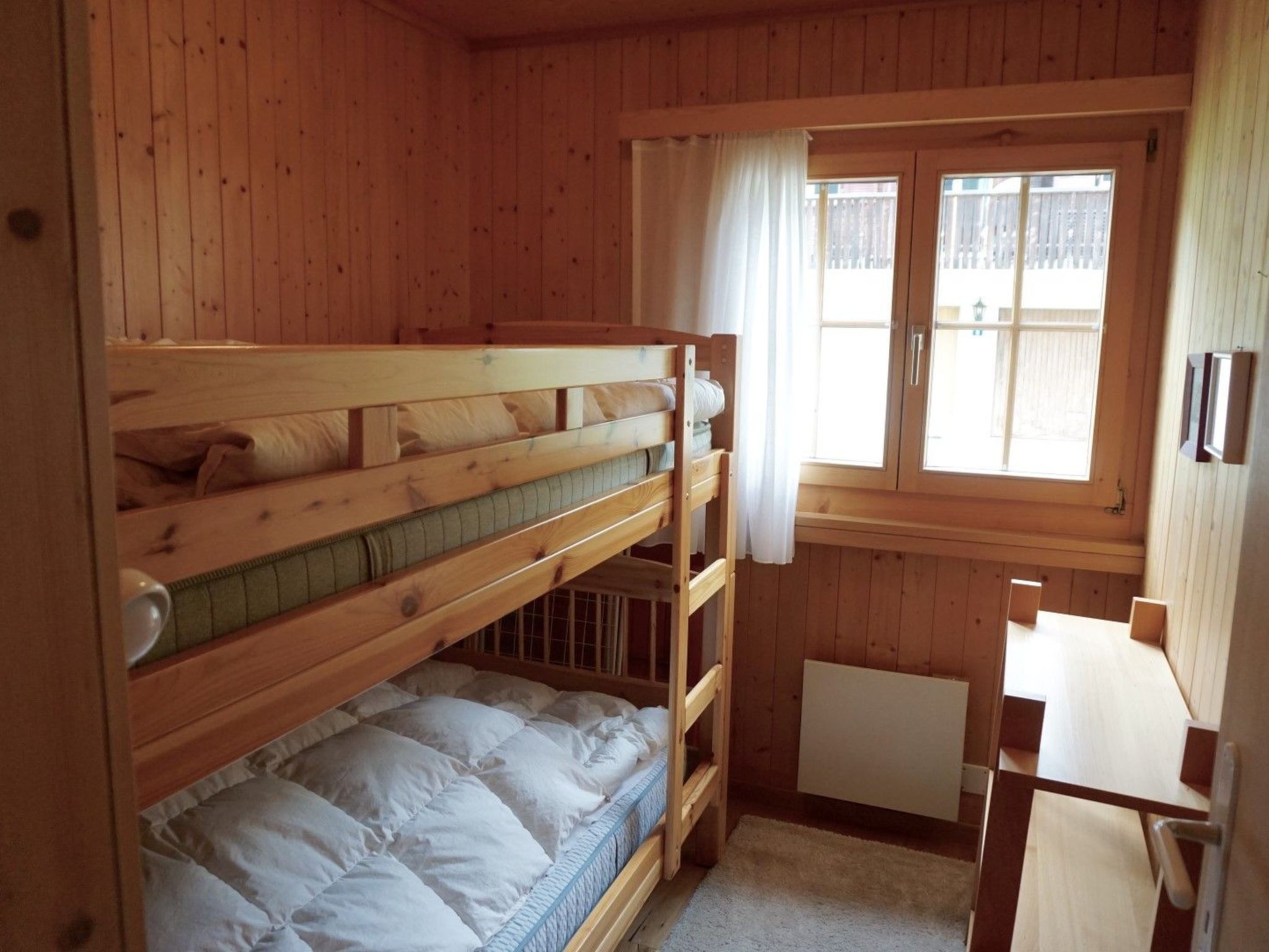 Een slaapkamer met stapelbed, een raam, houten wanden en een klein tafeltje.