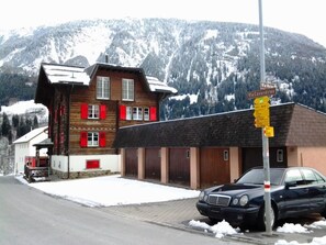 Ein Holzhaus mit roten Fensterläden, ein Auto davor und ein Berg im Hintergrund.