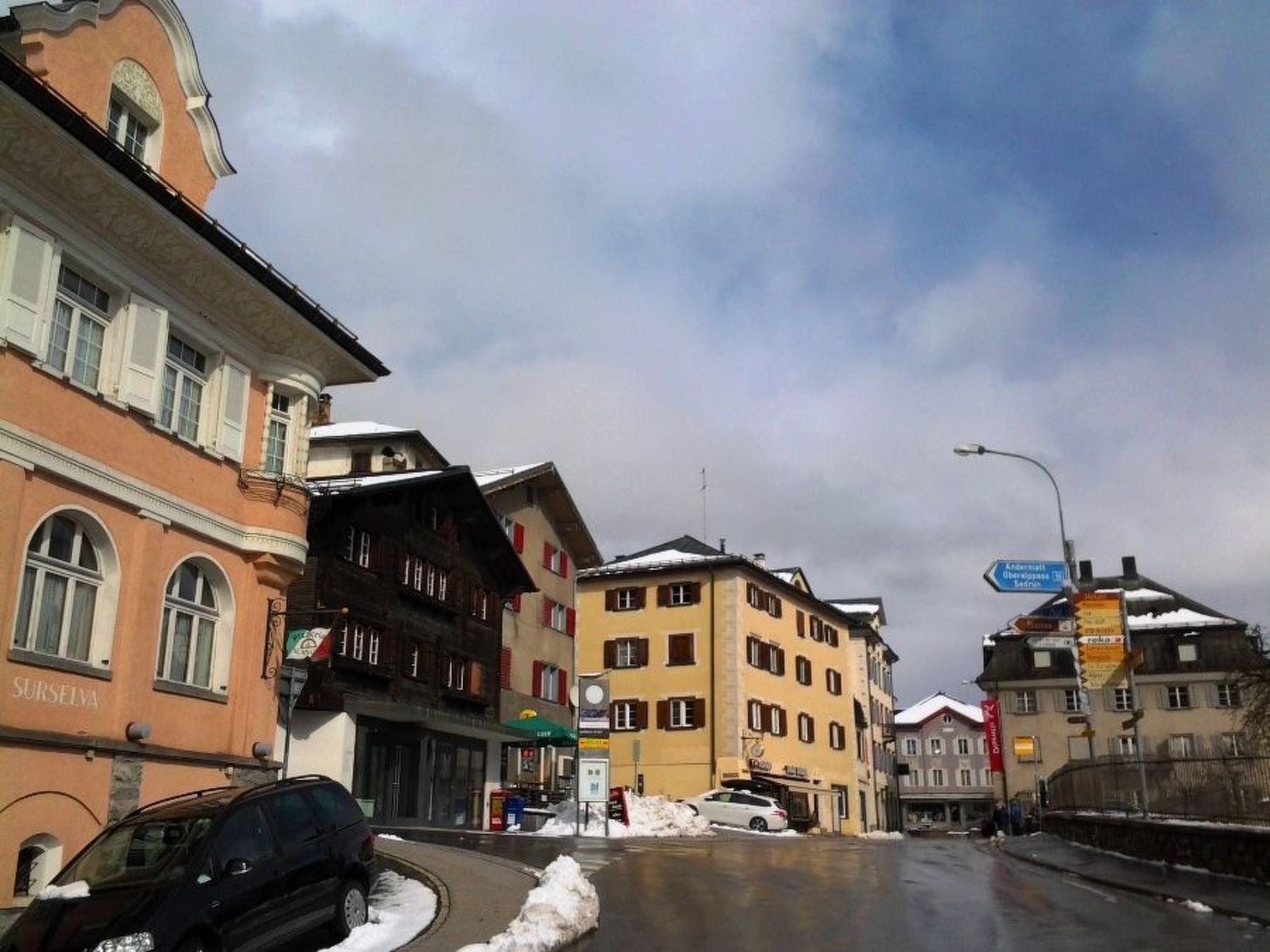 A street view with buildings, a car, and snow on the ground.