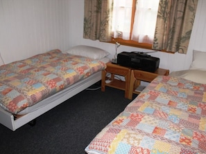 Een kleine kamer met twee eenpersoonsbedden, een nachtkastje met een radio en een raam met gordijnen.