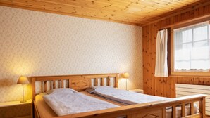 Une pièce en bois avec un lit, deux lampes de chevet, une fenêtre avec des rideaux et un banc en bois.
