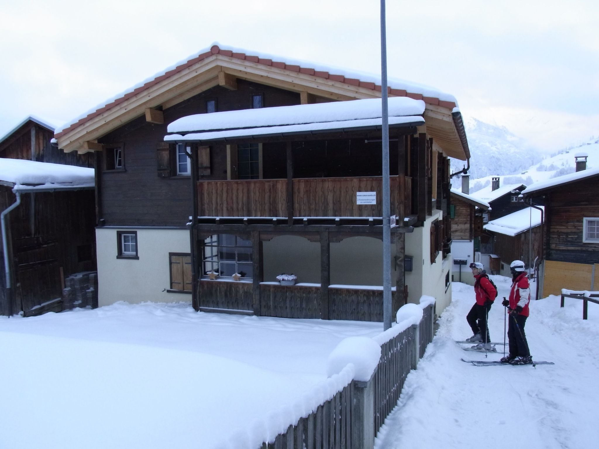A wooden chalet with a balcony, surrounded by snow-covered ground.