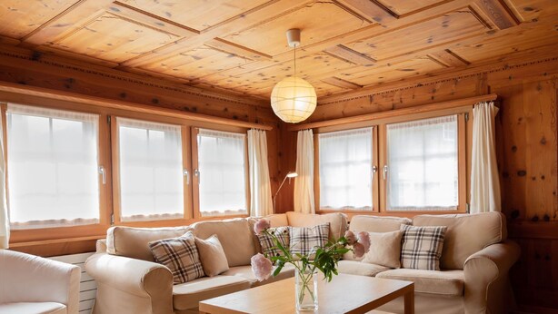 Un salon chaleureux avec un plafond en bois, un ensemble de canapés, une table basse et un vase rempli de fleurs.