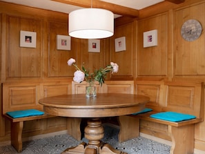 Ein Zimmer mit Holzwänden, einem runden Holztisch, blauen gepolsterten Bänken und einer weißen Pendelleuchte.