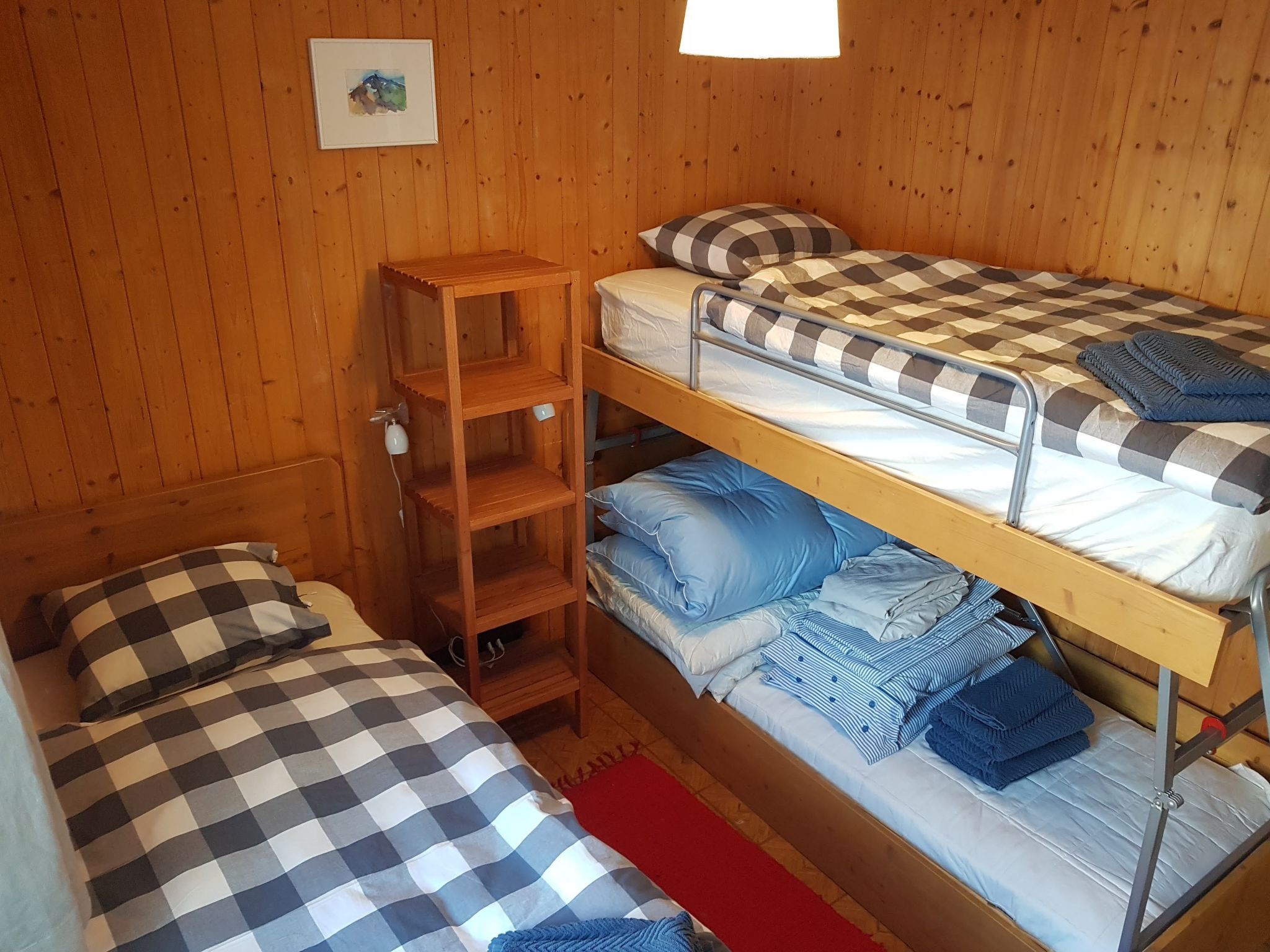 Een kamer met twee stapelbedden, een houten plankenwand en een rood vloerkleed.