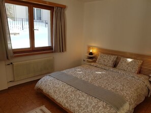 Ein Schlafzimmer mit einem Bett, einem Nachttisch, einem Fenster mit Vorhängen und einer Heizung.