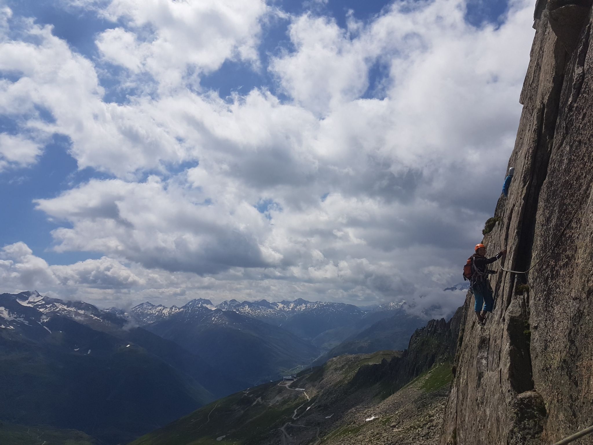 Una persona descendiendo en rápel por una pared rocosa escarpada, con un paisaje montañoso de fondo.