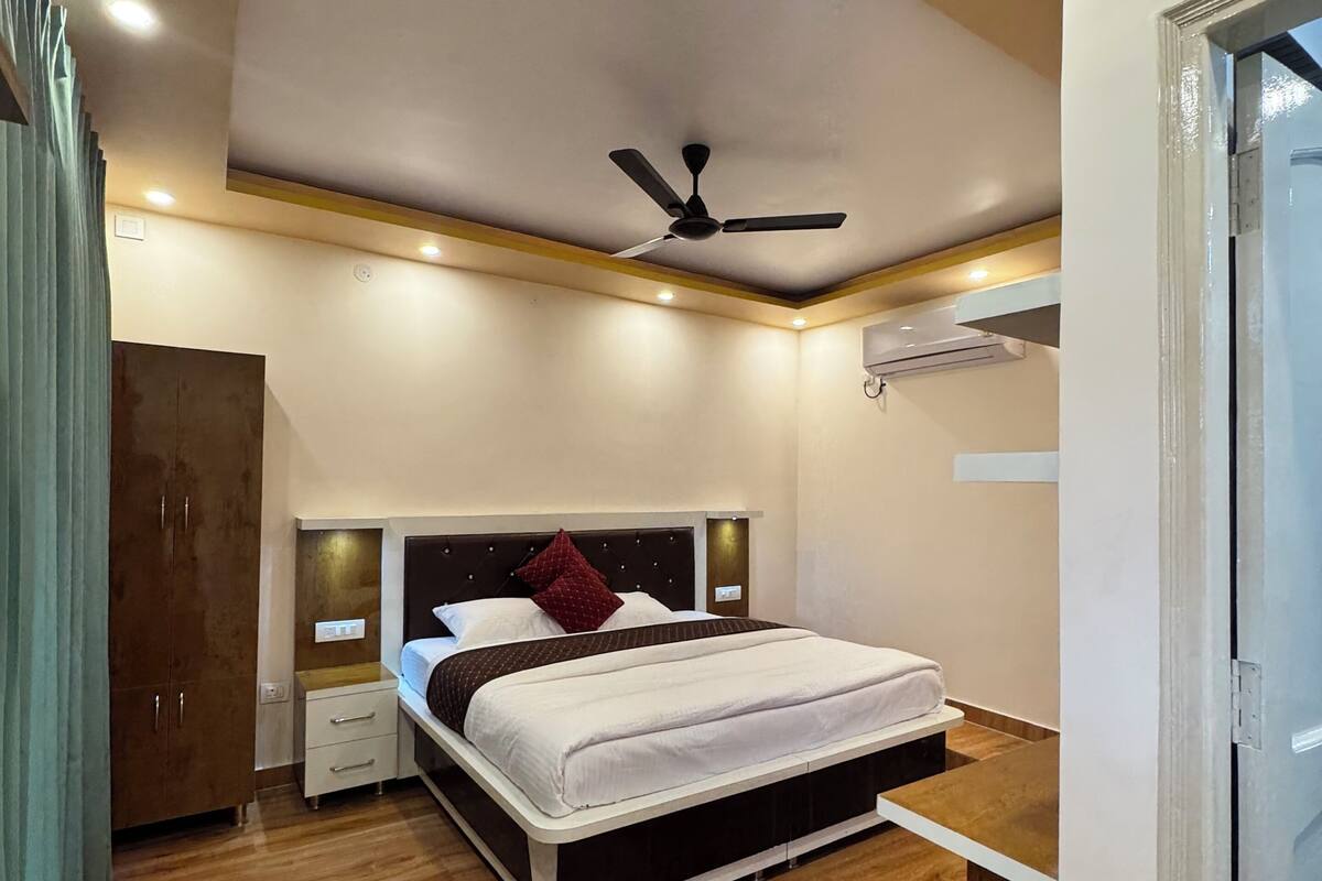 Une chambre moderne comprenant un lit, des tables de chevet, une armoire, un ventilateur de plafond, un éclairage encastré et un appareil de climatisation.
