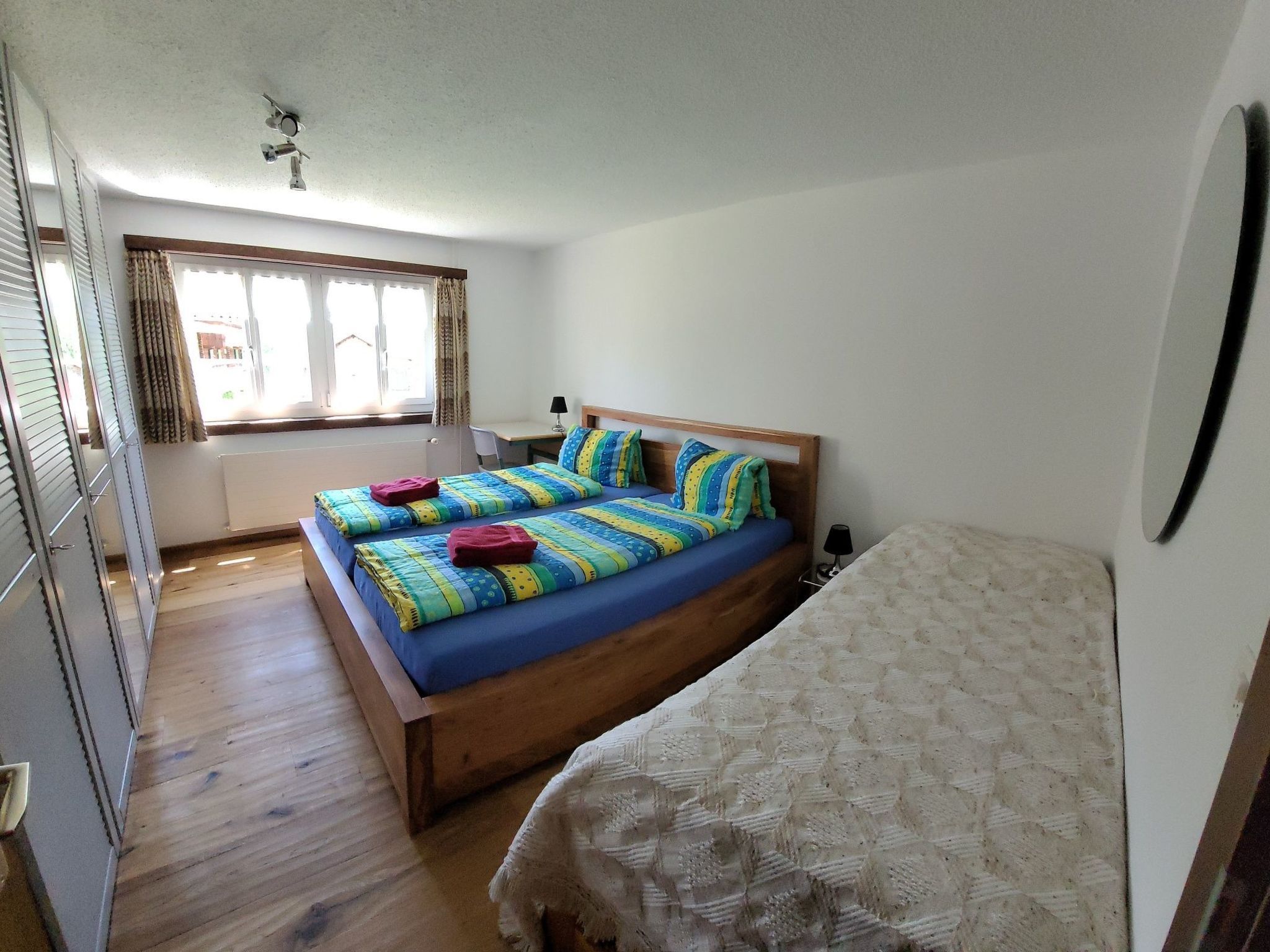 Une chambre à coucher avec un lit en bois, un plus petit lit et une fenêtre avec des rideaux.