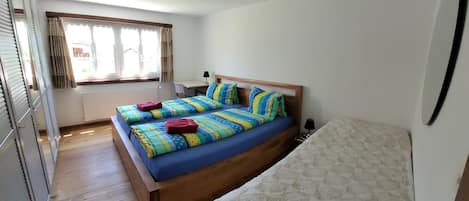 Une chambre à coucher avec un lit en bois, un plus petit lit et une fenêtre avec des rideaux.