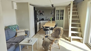 Un espacio habitable compacto con sofá, una mesita, una silla, una zona de cocina y una escalera.