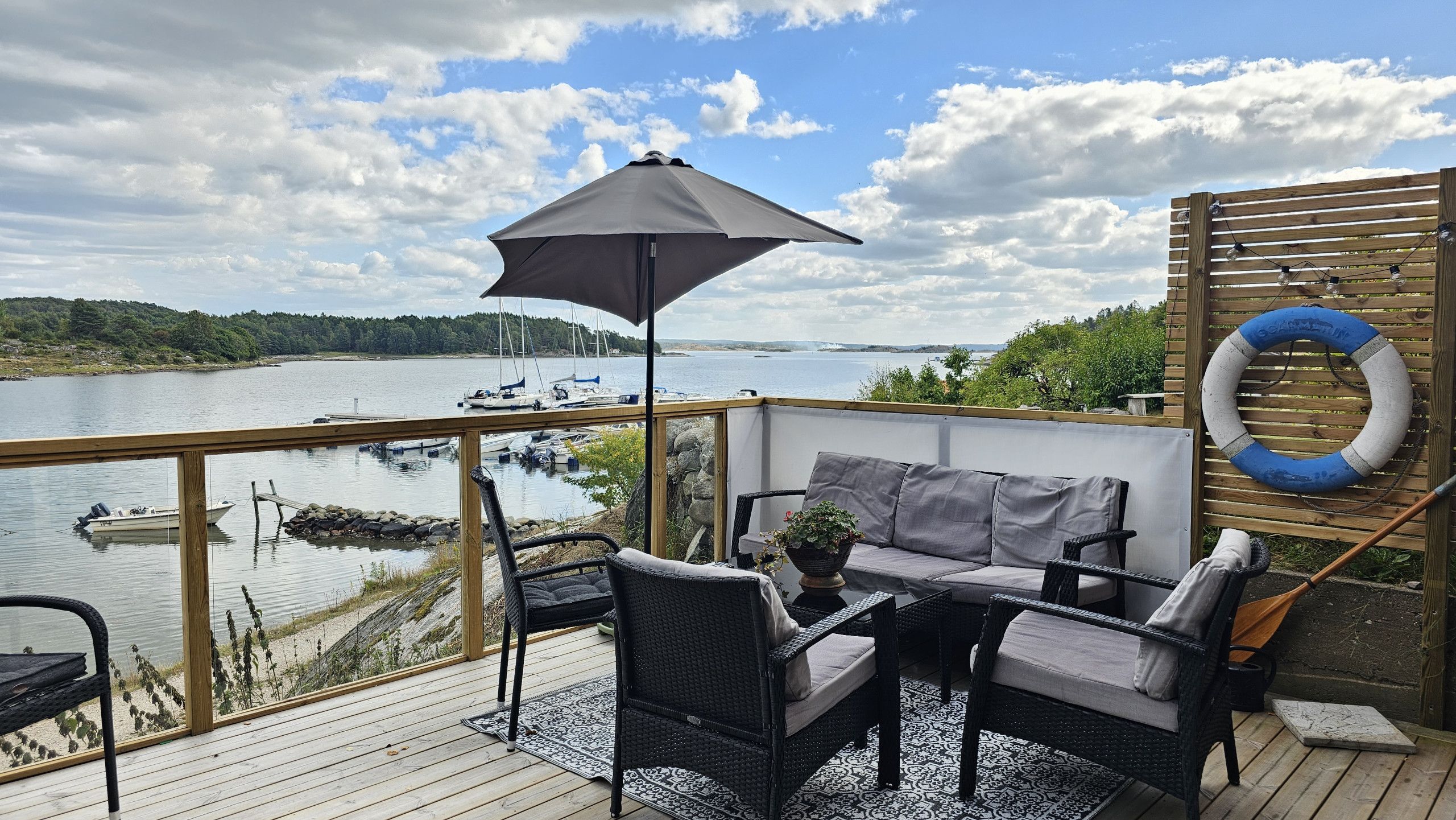 Une terrasse dotée de mobilier d’extérieur, offrant une vue sur l’eau et agrémentée d’une bouée de sauvetage fixée au mur.