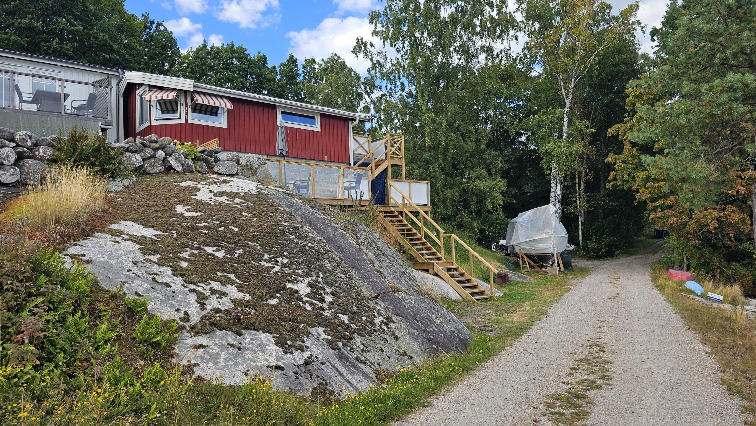 Ein Kiesweg führt zu einem roten Gebäude mit einer Holztreppe.