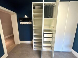 Een inloopkast met meerdere planken en knaagspullen, een kapstok en een klein plankje met decoratieve objecten.