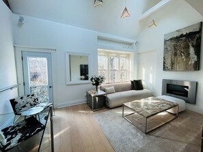 A modern living room with a sofa, coffee table, and a TV. There are windows, a door, and a painting on the wall. - Full Yorkville House w/ Spa, Gym, Office & Parking (Toronto)