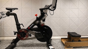 A stationary exercise bike with a digital display, positioned in a room with a tiled wall and a small wooden structure. - Full Yorkville House 3Bed w/ Spa, Gym, Parking (Toronto)
