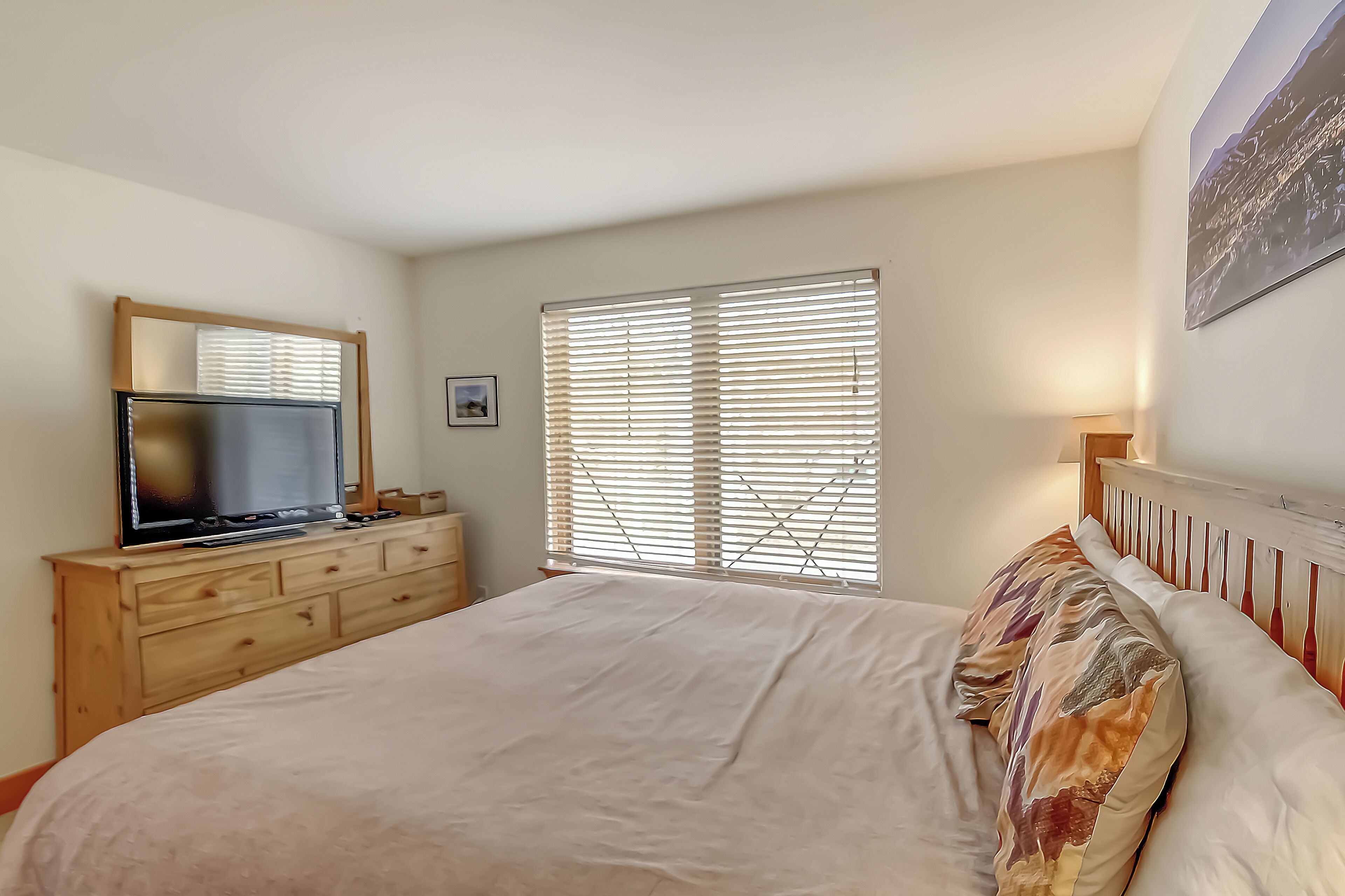 A bedroom with a bed, a dresser, a television, and a window with blinds.