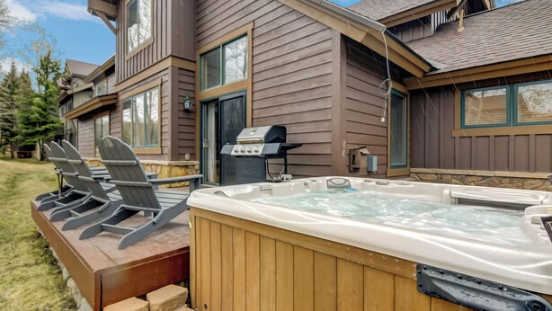 Ein Whirlpool mit Holzterrasse und Stühlen, ein Grill und ein Haus mit großen Fenstern.