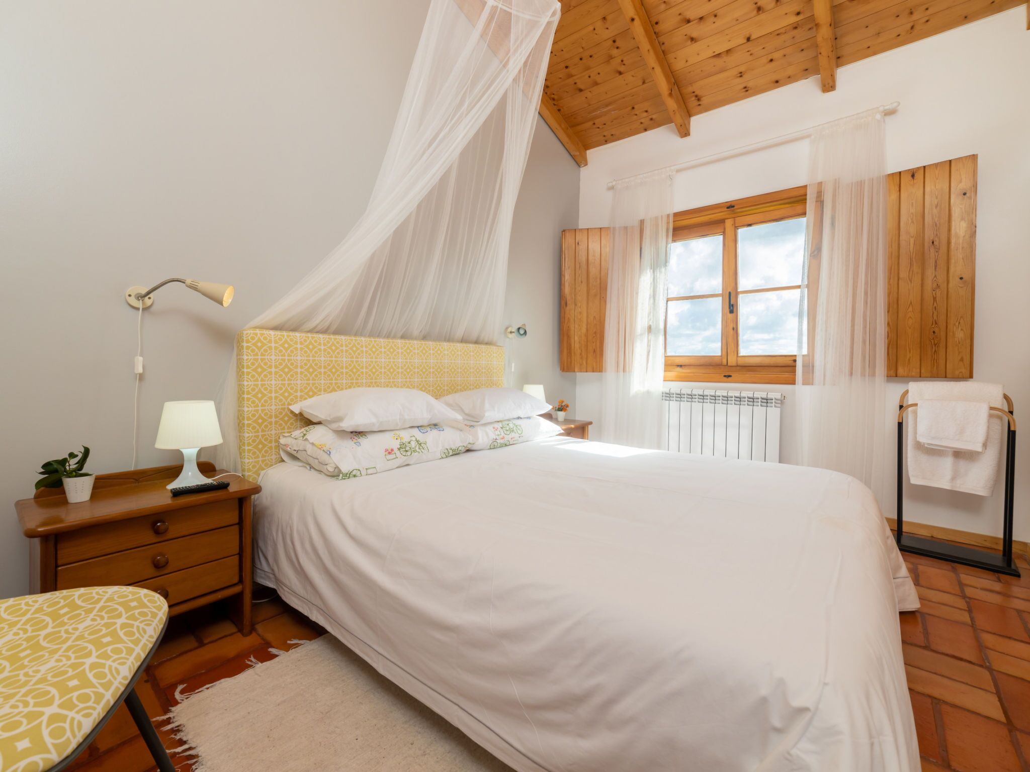 A bedroom with a bed, bedside table, lamp, and a window with curtains.