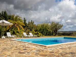 A swimming pool with stone flooring, surrounded by white lounge chairs and a palm tree. - MONTE CERRO DA VIGIA by Interhome (São Luís)