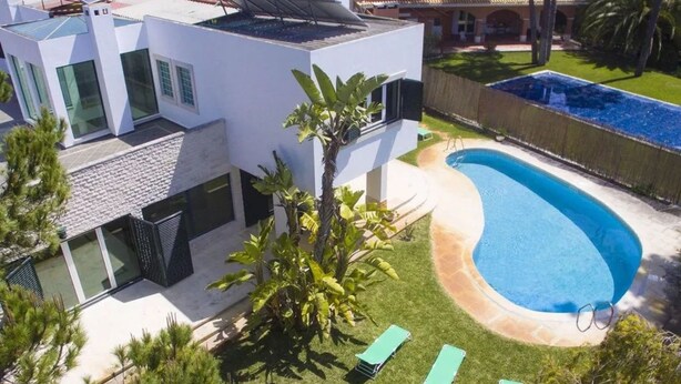Ett modernt hus med en swimmingpool, solpaneler och en välskött gräsmatta.