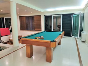 A pool table in a well-lit room with a tiled floor, large windows with blinds, and a sliding glass door. - VILLA FATI by Interhome (Tróia)