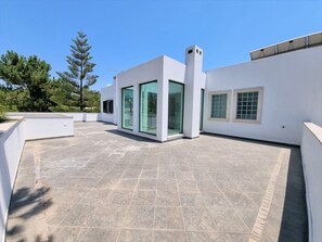 A modern building with a flat roof, large glass windows, and a tiled patio area. - VILLA FATI by Interhome (Tróia)