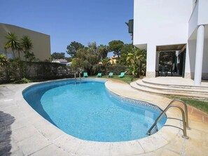 A swimming pool with a curved edge, surrounded by a paved deck and a small patio area with chairs. - VILLA FATI by Interhome (Tróia)