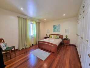 A bedroom with a wooden bed, a chair, a bedside table, a window with curtains, and a door with a handle. - VILLA FATI by Interhome (Tróia)
