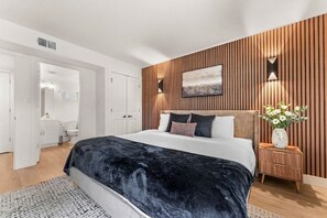 Een moderne slaapkamer met een groot bed, een wand van houten panelen en een klein nachtkastje met een bloevas.