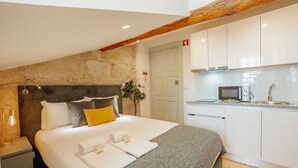A modern hotel room with a bed, a bedside table, a lamp, a plant, a kitchenette, and a stone wall. - Apartment  by Interhome (Porto)