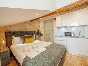 A modern hotel room with a bed, a bedside table, a lamp, a plant, a kitchenette, and a stone wall. - Apartment  by Interhome (Porto)