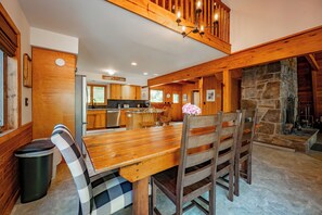 A wooden dining table with chairs, a kitchen area, and a stone fireplace. - New! Beautiful Lake Views and Lake Fun! (McHenry)