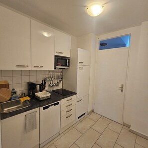 A compact kitchen with white cabinets, a microwave, a sink, and a window with a view. - Spacious, fully equipped apartment (Wien)
