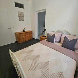 A bedroom with a bed, bedside table, lamp, dresser, and a door leading to another room. - Spacious, fully equipped apartment (Wien)