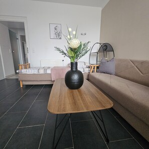 A living room with a sofa, a coffee table, a vase with flowers, a chair, and a radiator. - Spacious, fully equipped apartment (Wien)