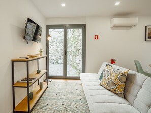 A modern living room with a sofa, a TV mounted on the wall, a bookshelf, and a view through a glass door to an outdoor area. - Apartment  by Interhome (Porto)