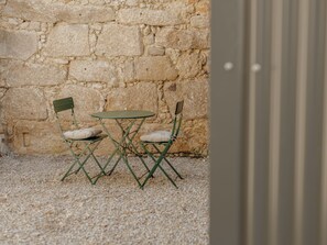 A small outdoor seating area with a stone wall backdrop, two green chairs with cushions, and a small round table. - Apartment  by Interhome (Porto)