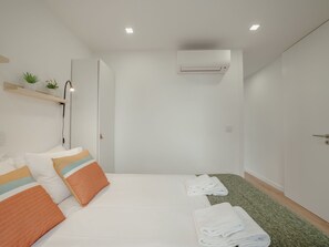 Et hotelværelse med en seng, et natbord, en vægmonteret aircondition og en lille hylde med planter.