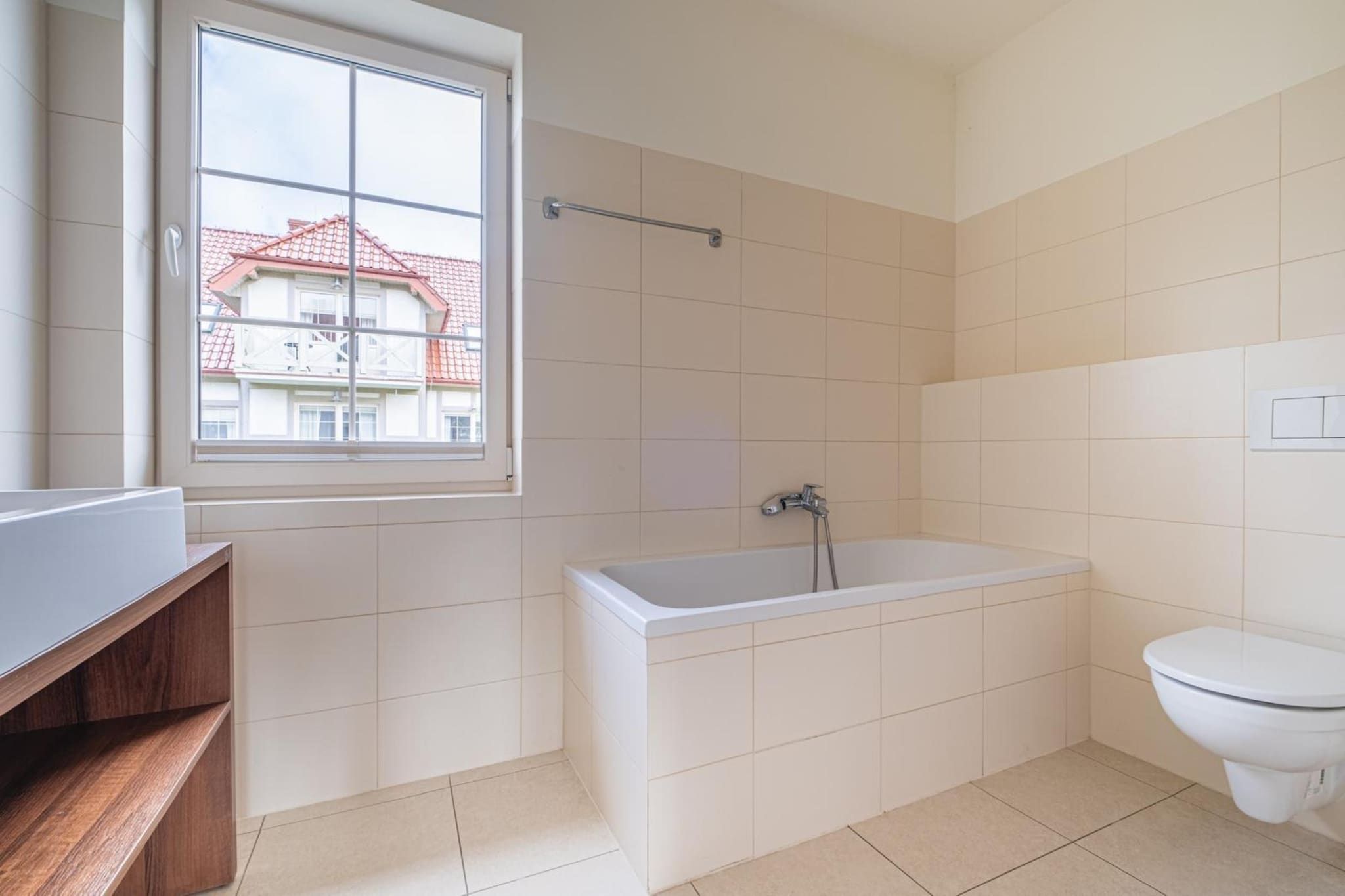 Een badkamer met een bad, toilet en een raam met uitzicht op gebouwen.