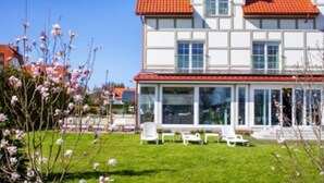 A two-story house with a red-tiled roof, large windows, and a covered patio area with outdoor furniture. - Beautiful and spacious apartment with a balcony (Debki)