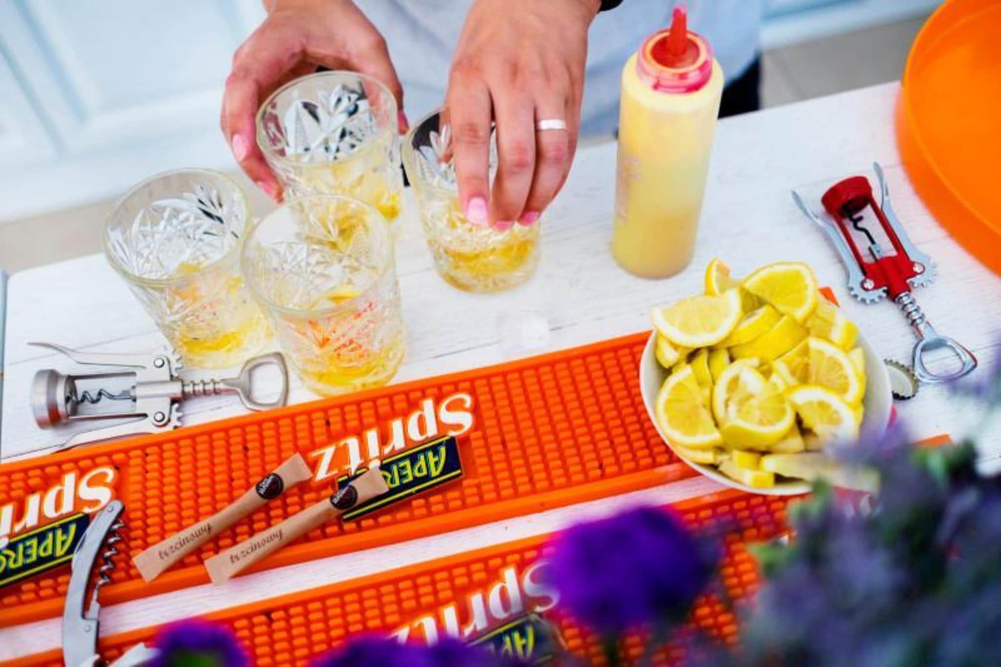 Una mesa con una botella de líquido amarillo, un plato de rodajas de limón, un abrelatas y un par de tijeras.