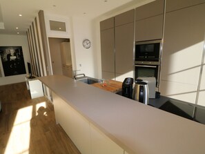 Une cuisine moderne avec un long plan de travail, un four encastré et une horloge au mur.