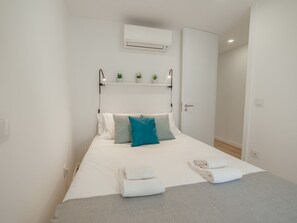 Ein Hotelzimmer mit Bett, Nachttisch, Wandklimaanlage und einer kleinen Ablage mit Blumentöpfen.