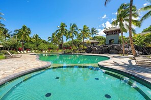 A swimming pool with a curved design, surrounded by palm trees and a small building with a tiled roof. - NEW! Mauna Lani Beach Club Pass/BBQ on lanai/602 Fairways at Mauna Lani (Kamuela)
