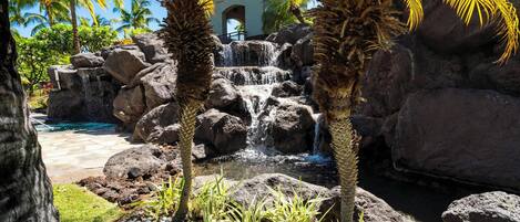A tropical garden with a waterfall, palm trees, and a pool.