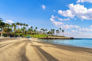 A beach with rows of sun loungers and palm trees, a stone wall, and a clear blue sky. - NEW! Mauna Lani Beach Club Pass/BBQ on lanai/602 Fairways at Mauna Lani (Kamuela)